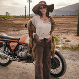 Person in vintage attire standing next to a motorcycle in an open field with mountains in the background wearing Soul Sister since 1969