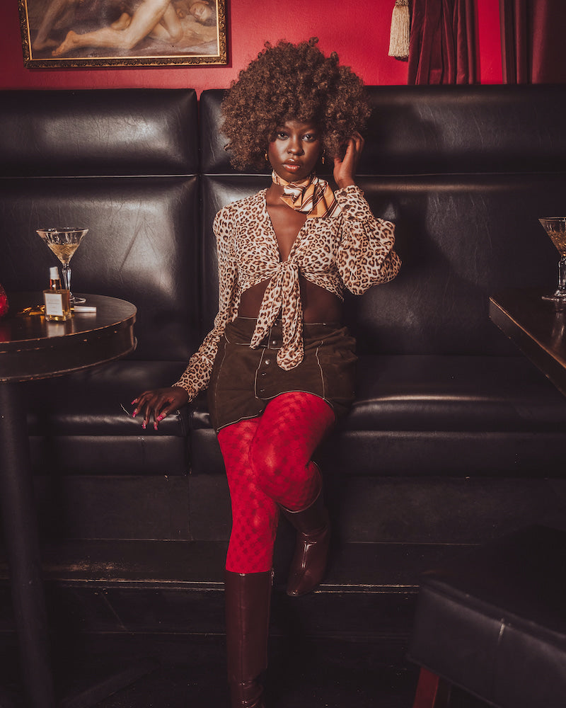 Woman in a leopard print top and red stockings sitting on a black leather couch in a bar.