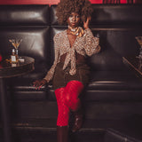 Woman in a leopard print top and red stockings sitting on a black leather couch in a bar.