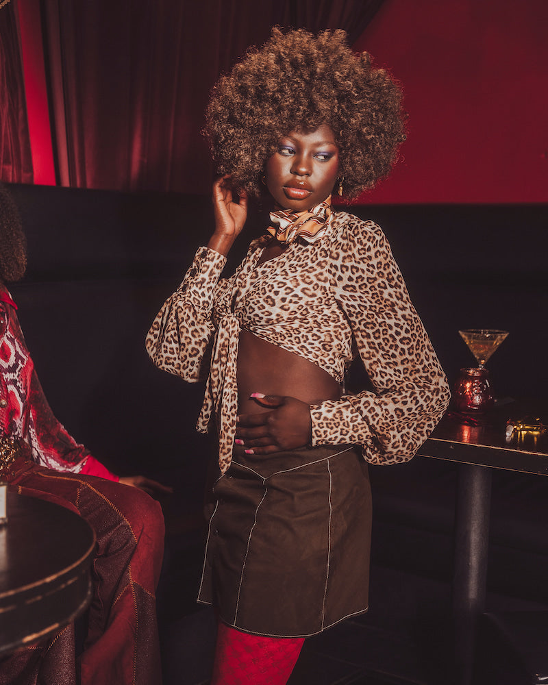 Woman in leopard print top and brown skirt in a dimly lit room with red accents