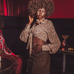 Woman in leopard print top and brown skirt in a dimly lit room with red accents