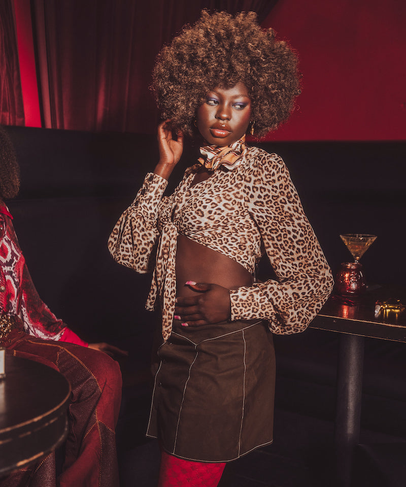 Woman in leopard print top and brown skirt in a dimly lit room with red accents