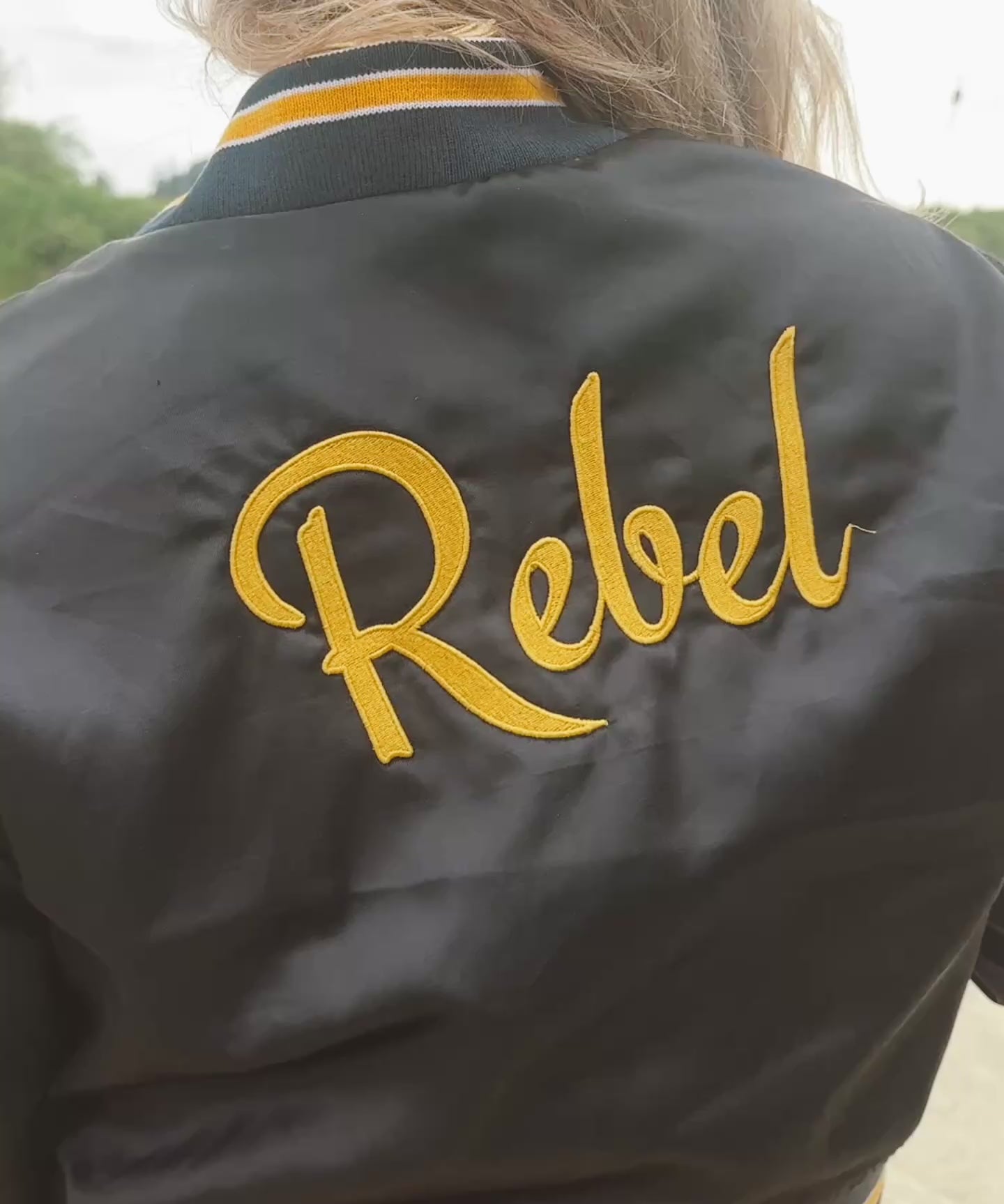 model wears satin bomber jacket with the words Rebel on the back
