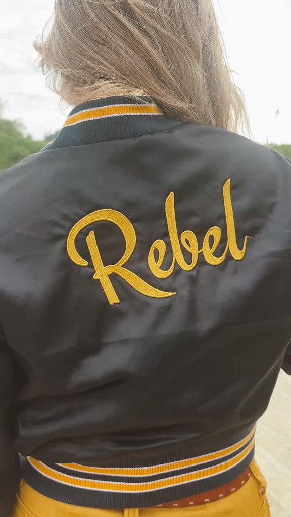 model wears satin bomber jacket with the words Rebel on the back
