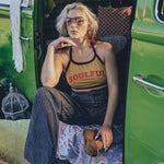 A person wearing a yellow halter top with the word 'SOUULFUL' printed on it, sitting in a green vehicle with their legs dangling outside.