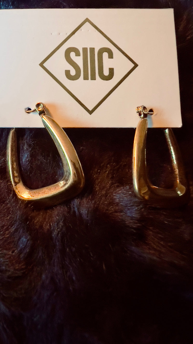 Gold hoop earrings on a card with 'SIIC' branding, displayed on a dark fur surface.