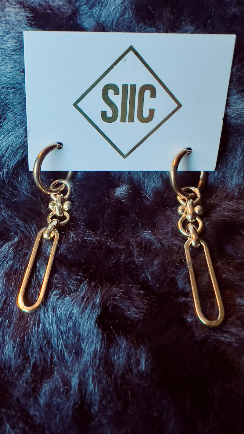 Gold earrings on a card with 'SIIC' branding against a dark fur background