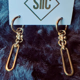 Gold earrings on a card with 'SIIC' branding against a dark fur background