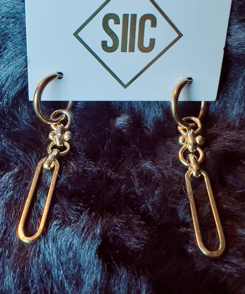 Gold earrings on a card with 'SIIC' branding against a dark fur background