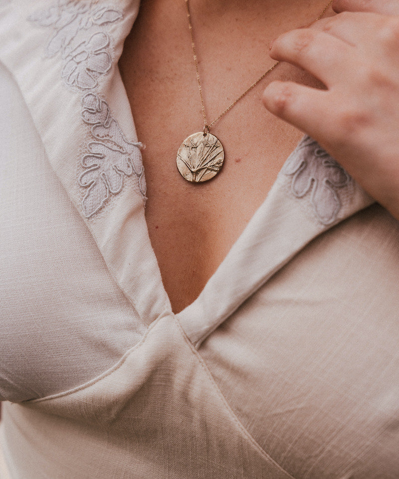 Close-up of a person wearing a gold necklace with a circular pendant. wearing Soul Sister since 1969
