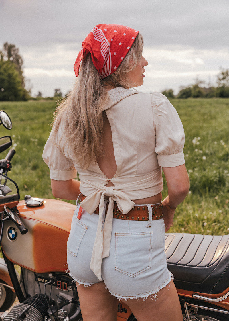 Woman with a red bandana standing next to a motorcycle in a field wearing Soul Sister since 1969