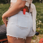 Person wearing light blue denim shorts with a red tool in the pocket, standing outdoors wearing Soul Sister since 1969.