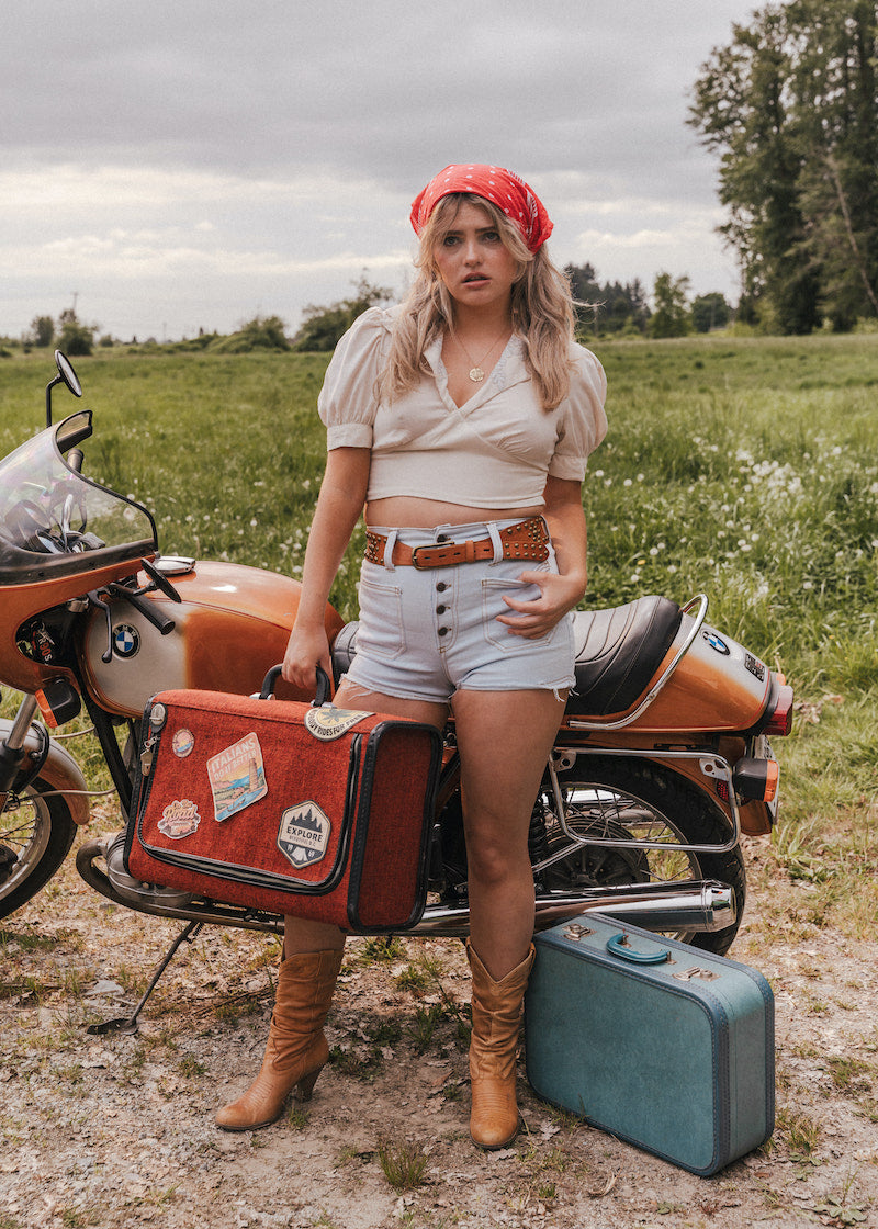 Woman standing next to a motorcycle with a suitcase in a field wearing Soul Sister since 1969

