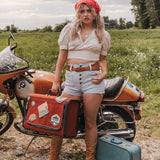 Woman standing next to a motorcycle with a suitcase in a field wearing Soul Sister since 1969.
