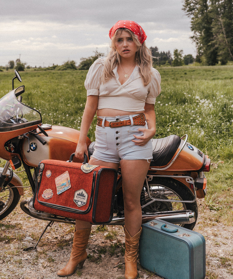 Woman standing next to a motorcycle with a suitcase in a field wearing Soul Sister since 1969.