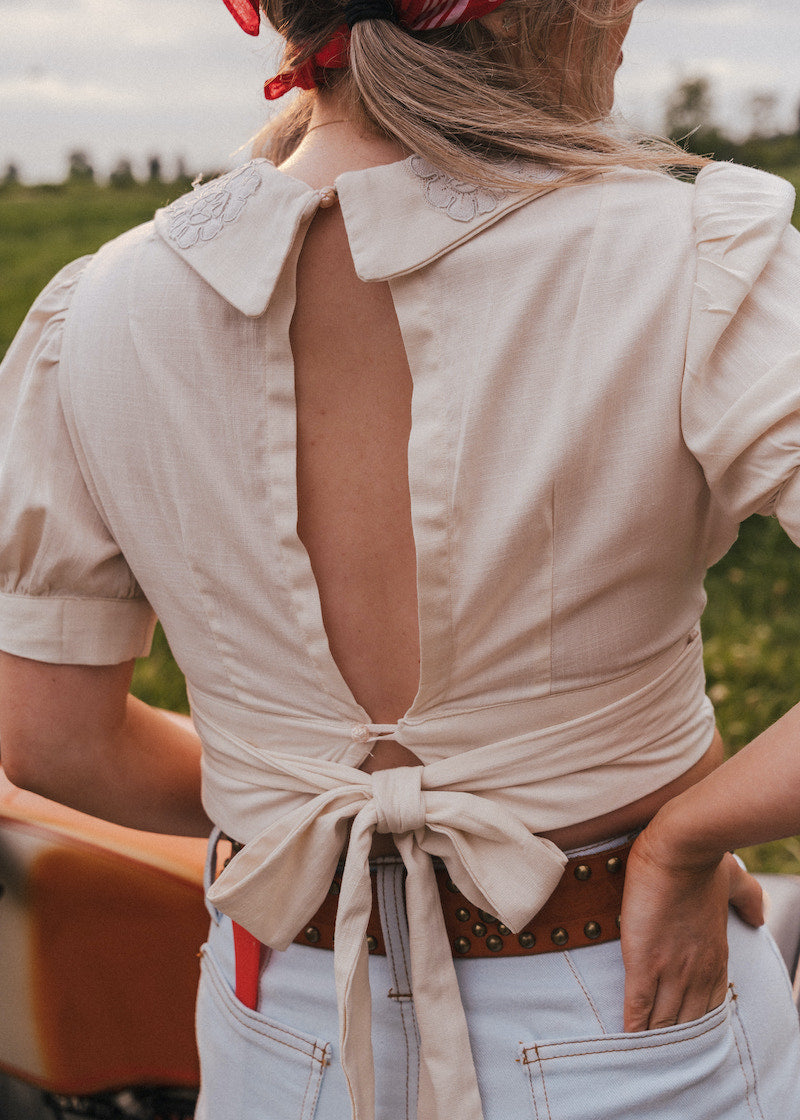 Woman wearing a beige open-back shirt with a field in the background wearing Soul Sister since 1969