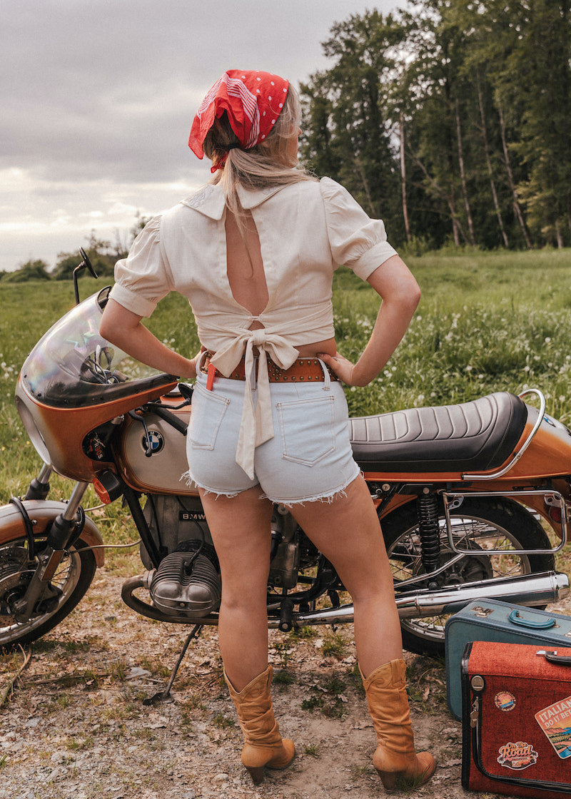Person standing next to a motorcycle in a field with a red bandana and open back top wearing Soul Sister since 1969..